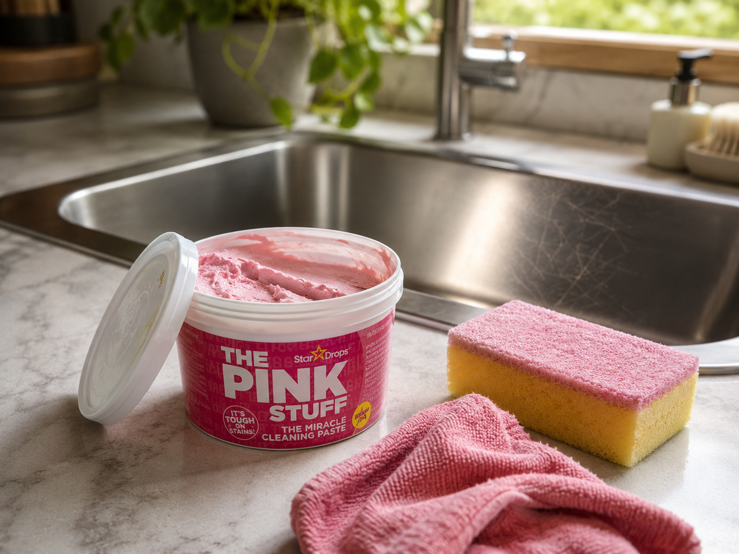 Open tub of pink paste cleaner next to sponge and kitchen sink