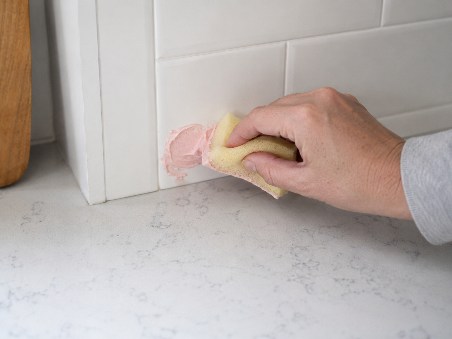 Close-up of a hand testing a pink paste on a small corner of glossy tile with a sponge